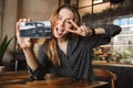 Emotional happy beautiful young pretty woman sitting in cafe indoors using mobile phone talking with friends take a selfie Royalty Free Stock Photo