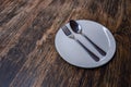 Photo of an empty white plate with spoon and fork on a rustic wooden table.White plates and cutlery on wooden table. copy space