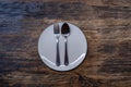 Photo of an empty white plate with spoon and fork on a rustic wooden table.White plates and cutlery on wooden table. copy space