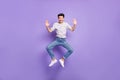 Photo of energetic active guy jump raise palms wear white striped t-shirt jeans footwear isolated purple background