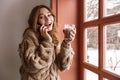 Photo of european woman 20s with brown hair talking on smartphone near window, and drinking glass of latte in cafe Royalty Free Stock Photo