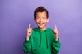 Photo of excited charming little boy dressed green hoodie showing two fingers up empty space isolated purple color