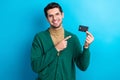 Photo of excited cheerful man wear green cardigan arm spectacles showing finger bank card isolated blue color background Royalty Free Stock Photo
