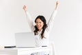 Photo of excited chinese businesswoman with long dark hair screaming with raised arms and celebrating success while working in Royalty Free Stock Photo