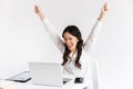 Photo of excited chinese businesswoman with long dark hair screaming with raised arms while working with documents and laptop, is Royalty Free Stock Photo