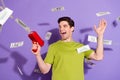 Photo of excited funky young man guy wear green t-shirt shooting money gun smiling isolated violet color background