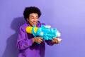 Photo of excited funny guy afro hairdo dressed purple pullover hold water gun look empty space isolated on violet color