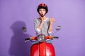 Photo of excited girl ride motorbike indicate thumb empty space palm cheek wear helmet striped shirt isolated purple Royalty Free Stock Photo