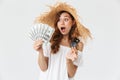 Photo of excited gorgeous woman 20s wearing big straw hat holding credit card and fan of dollar banknotes, isolated over white ba Royalty Free Stock Photo