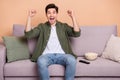 Photo of excited guy sit couch watch world cup match fist-up enjoy national team win isolated over beige color