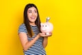 Photo of excited impressed woman dressed striped t-shirt holding money box looking empty space isolated yellow color Royalty Free Stock Photo