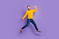 Photo of excited man jump run raise hands wear yellow pullover jeans footwear isolated violet background Royalty Free Stock Photo