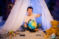 Photo of excited surprised kid boy pointing globe choose summer holiday trip in evening playroom nursery Royalty Free Stock Photo