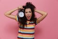 Photo of excited woman 20s with curly hair holding alarm clock,