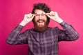 Photo of excited young bearded hipster man touching his round glasses and looking confident at the camera Royalty Free Stock Photo