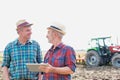 Farmers using digital tablet while standing against tractor in field