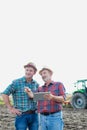 Farmers using digital tablet while standing against tractor in field