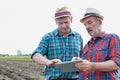 Farmers using digital tablet while standing against tractor in field