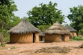 A photo featuring a dirt field with a couple of huts, showcasing the simple dwellings on a rustic landscape, A traditional African