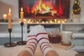 Photo of feet in striped socks on side table with candles, teapot and cup  bevor fireplace imitation Royalty Free Stock Photo