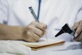 Female doctor with otoscope in hand writing prescription