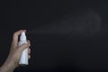 Female hand holding white sprey bottle and spray on dark background Royalty Free Stock Photo