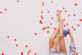 Photo of female legs on red confetti. European girl holding blue cup of beverage..