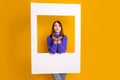 Photo of flirty cute young woman wear purple pullover holding big white paper photo frame isolated yellow color Royalty Free Stock Photo