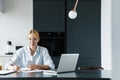 Photo of focused young woman working with cellphone and laptop