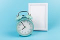 Photo frame and blue alarm clock on blue background with copy space Royalty Free Stock Photo