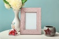 Photo frame with flowers in vase and candle holder on white table against color background Royalty Free Stock Photo