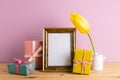 Photo frame with gift boxes and yellow tulip on wooden table with pink background Royalty Free Stock Photo