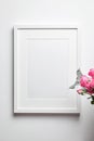 Photo frame mockup with passe-partout hanging on white wall and and bouquet of pink roses with eucalyptus. Empty blank frame and Royalty Free Stock Photo