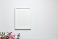 Photo frame mockup with passe-partout hanging on white wall and and bouquet of pink roses with eucalyptus. Empty blank frame and Royalty Free Stock Photo