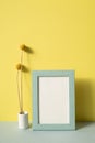 Photo frame with vase of dry flower on gray shelf. yellow wall background Royalty Free Stock Photo