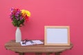 Photo Frame on a wooden table and book and Flowers in jar on pink background .