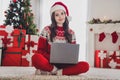 Photo of freelancer lovely lady sit carpet typing netbook wear santa hat sweater pants socks in decorated home indoors