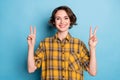 Photo of friendly charming girl show two v-signs white smile wear checkered shirt isolated blue color background