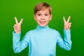 Photo of friendly funny small son wear turquoise turtle neck showing two v-signs green color background