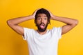 Photo of frightened dark skin guy open mouth awful news arms on head wear t-shirt isolated yellow color background