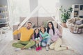 Photo of full family four members two little kids parents hold roof sit floor wear colorful sweater in living room Royalty Free Stock Photo