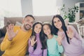 Photo of full family four people two small children waving hand look camera wear colorful pullover in living room