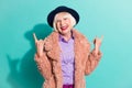 Photo of funky adorable old woman dressed vintage outerwear cap showing hard rock sign isolated turquoise color Royalty Free Stock Photo