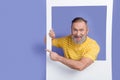 Photo of funky cheerful retired man dressed striped t-shirt hold frame directing at promo empty space isolated on purple