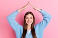 Photo of funky cheerful young woman dressed blue cardigan showing roof overhead smiling isolated on pink color