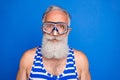 Photo of funky funny mature man in swimming goggles wear striped swim suit isolated on blue color background Royalty Free Stock Photo