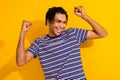 Photo of funky man with dreadlocks dressed striped t-shirt win bet raising fists up eyes closed isolated on yellow color