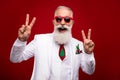 Photo of funky old grey hair man show v-sign wear eyewear white jacket isolated on red color background Royalty Free Stock Photo