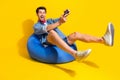 Photo of funky positive guy wear jeans jacket shorts sit on pouf hold playstration joystick isolated on bright yellow