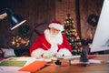 Photo of funky positive santa claus wear red costume writing christmas greetings indoors north pole office Royalty Free Stock Photo